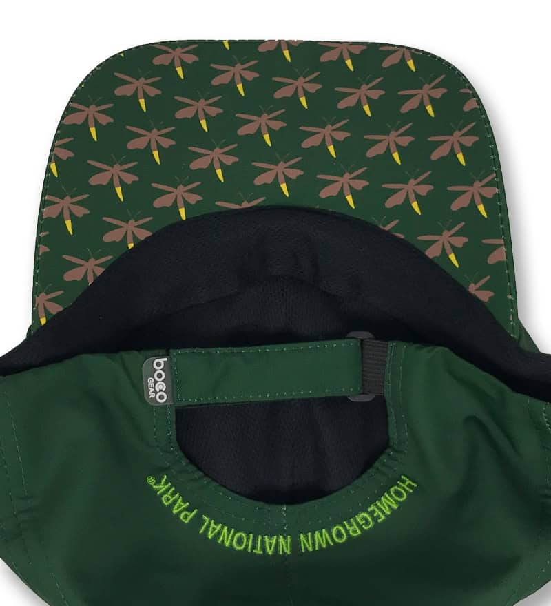 Green cap with "Homegrown National Park" embroidered in yellow, featuring a patterned brim with dragonflies in brown and yellow on a dark green background. Perfect for eco-conscious outdoor enthusiasts.